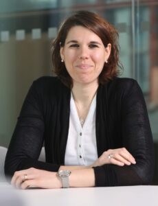 CellRev's Chief Scientific Officer, Martina Miotto, smiles at the camera while sitting at a desk with her arms lightly folded, wearing a white shirt and black jacket.